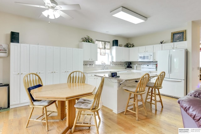 kitchen with a kitchen breakfast bar, a center island, white cabinets, white appliances, and light wood-style flooring