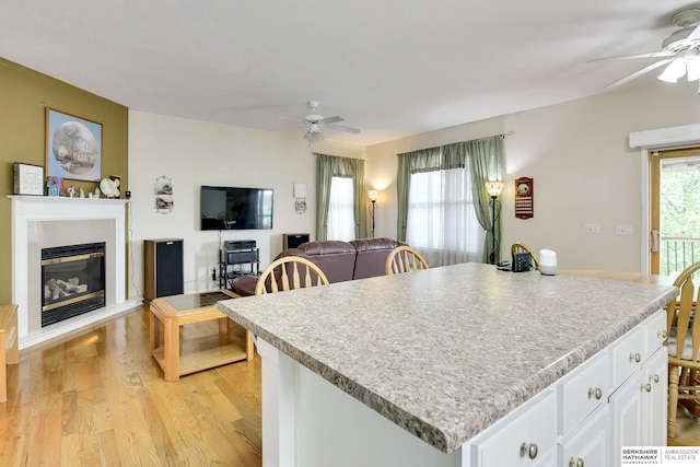 kitchen featuring ceiling fan, a center island, light countertops, white cabinets, and light wood-style flooring