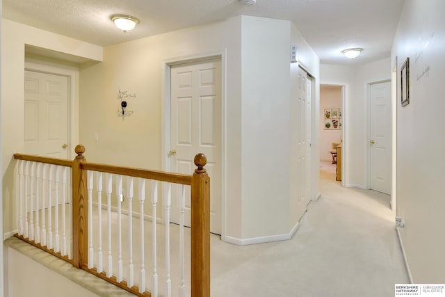 corridor with light colored carpet, baseboards, and an upstairs landing