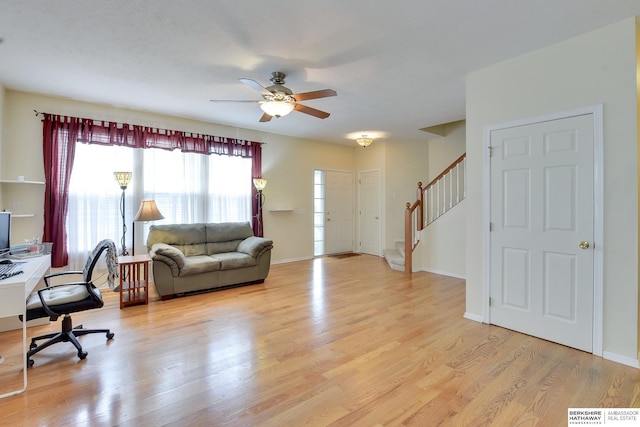 living area featuring stairway, baseboards, ceiling fan, and light wood-style flooring