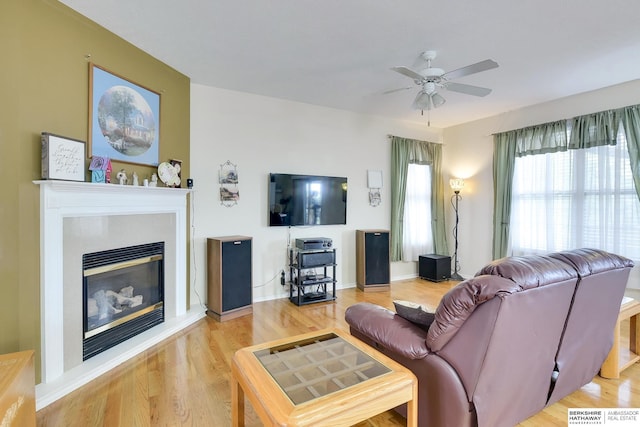 living room with a glass covered fireplace, ceiling fan, and wood finished floors
