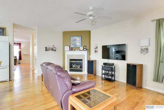 living area featuring visible vents, a glass covered fireplace, light wood-style floors, baseboards, and a ceiling fan