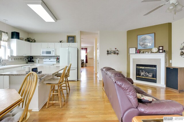 living room featuring light wood-style floors, a glass covered fireplace, and ceiling fan