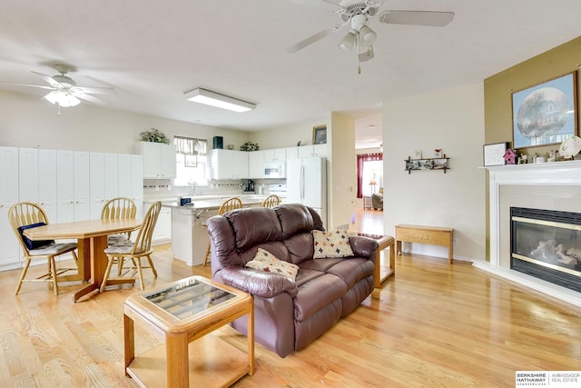 living room featuring light wood-style floors, a ceiling fan, and a glass covered fireplace