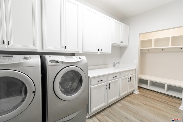 washroom with cabinet space, washing machine and dryer, a sink, and light wood-style floors