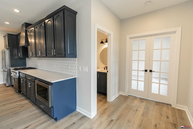kitchen with wall chimney range hood, backsplash, french doors, light wood-type flooring, and stainless steel appliances