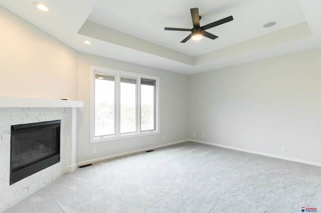 unfurnished living room featuring visible vents, ceiling fan, a tray ceiling, carpet flooring, and a premium fireplace