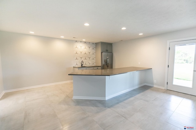 kitchen featuring a peninsula, baseboards, stainless steel refrigerator with ice dispenser, recessed lighting, and a sink