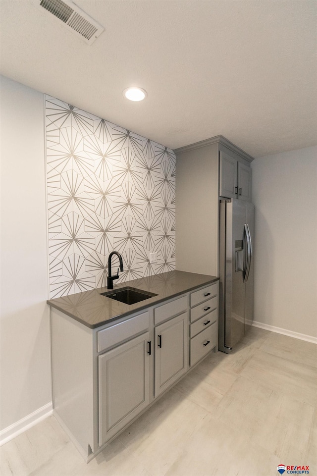 kitchen featuring stainless steel refrigerator with ice dispenser, baseboards, dark countertops, and a sink