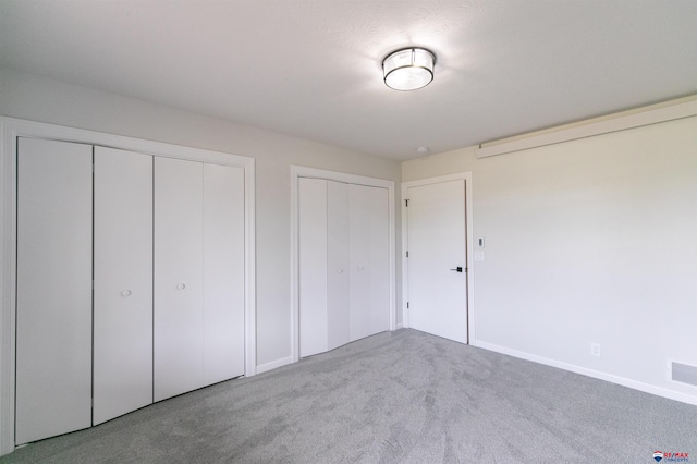 unfurnished bedroom featuring two closets, baseboards, and carpet floors