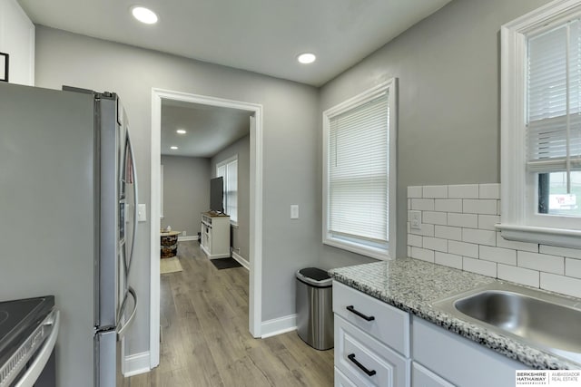 kitchen featuring decorative backsplash, white cabinetry, a sink, light wood finished floors, and appliances with stainless steel finishes