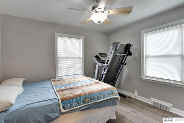 bedroom featuring baseboards, visible vents, multiple windows, and wood finished floors