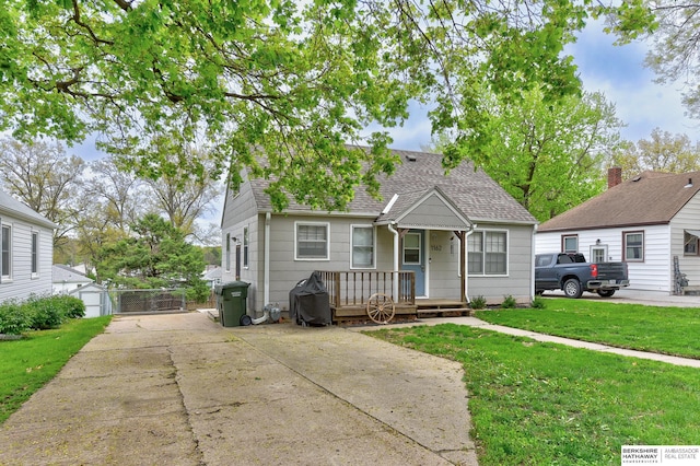 view of front facade with roof with shingles, driveway, and a front yard