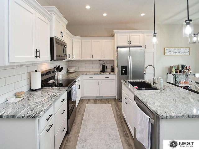 kitchen with appliances with stainless steel finishes, a sink, recessed lighting, white cabinetry, and wood finished floors