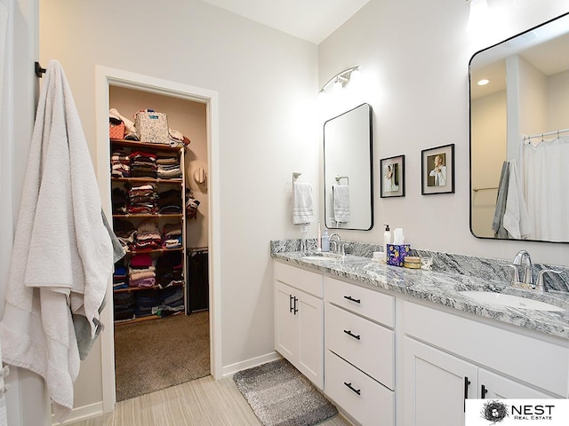bathroom with double vanity, baseboards, a spacious closet, and a sink