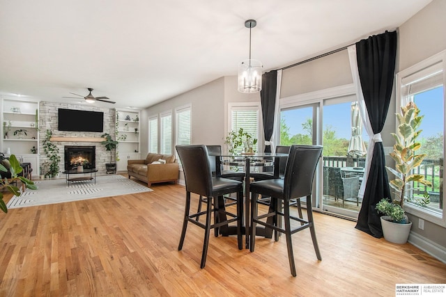 dining area featuring a ceiling fan, visible vents, built in features, a fireplace, and light wood finished floors