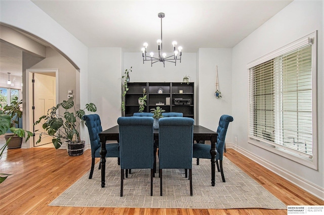 dining room featuring arched walkways, baseboards, a chandelier, and light wood-type flooring