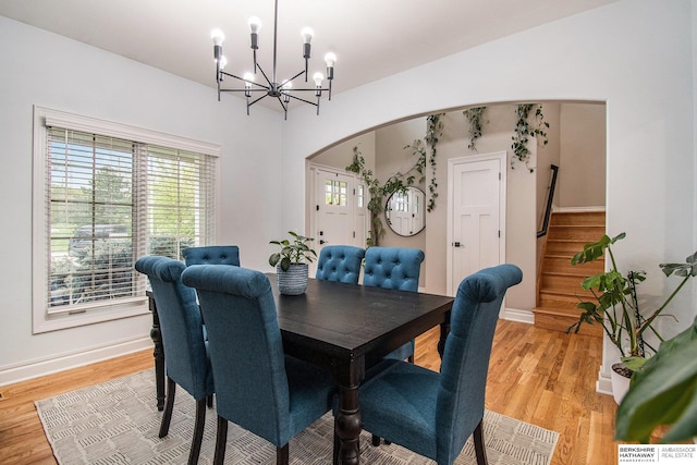 dining space with arched walkways, light wood-type flooring, stairs, and a chandelier