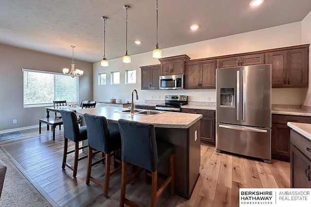 kitchen with dark brown cabinetry, a breakfast bar, light countertops, a sink, and appliances with stainless steel finishes