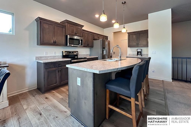 kitchen with a kitchen breakfast bar, appliances with stainless steel finishes, dark brown cabinets, a sink, and light countertops
