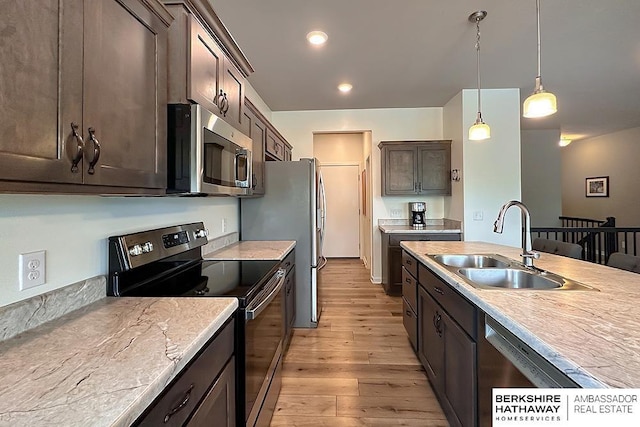 kitchen with dark brown cabinetry, a sink, light wood-style flooring, appliances with stainless steel finishes, and hanging light fixtures