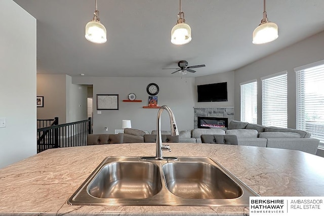 kitchen with a ceiling fan, a glass covered fireplace, open floor plan, a sink, and hanging light fixtures