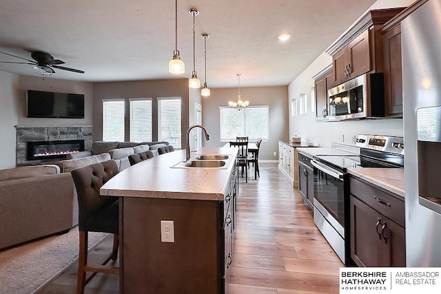 kitchen with a kitchen breakfast bar, appliances with stainless steel finishes, a sink, ceiling fan with notable chandelier, and a glass covered fireplace