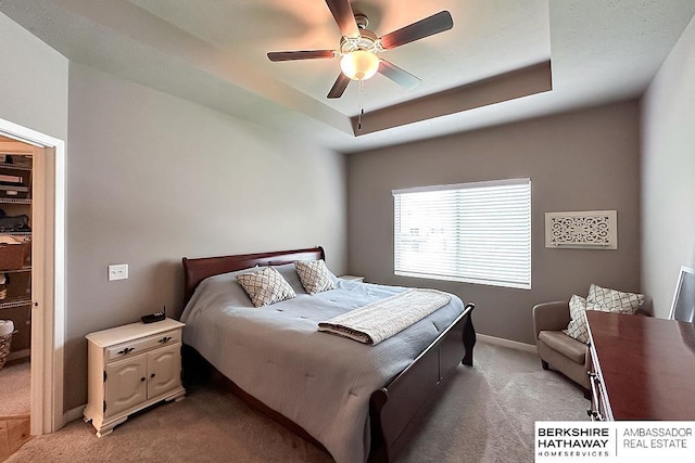 bedroom with ceiling fan, light colored carpet, baseboards, and a raised ceiling