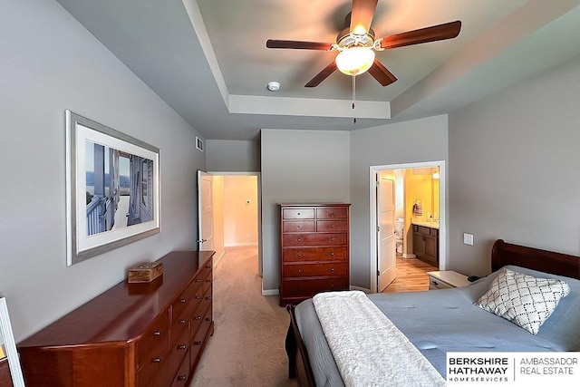 bedroom with visible vents, light carpet, connected bathroom, a raised ceiling, and a ceiling fan