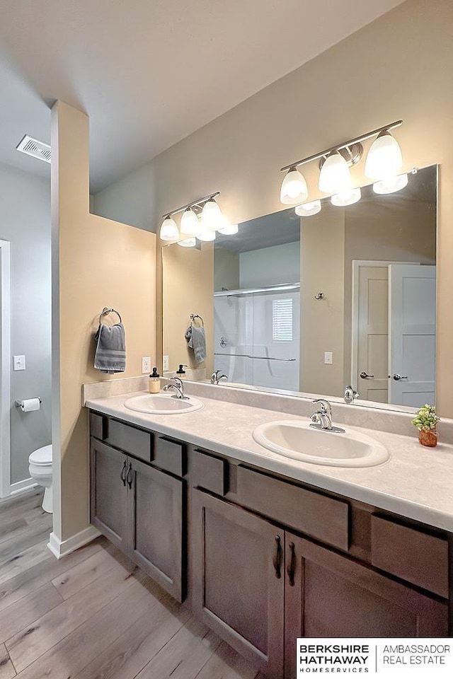 bathroom with a sink, toilet, wood finished floors, and visible vents