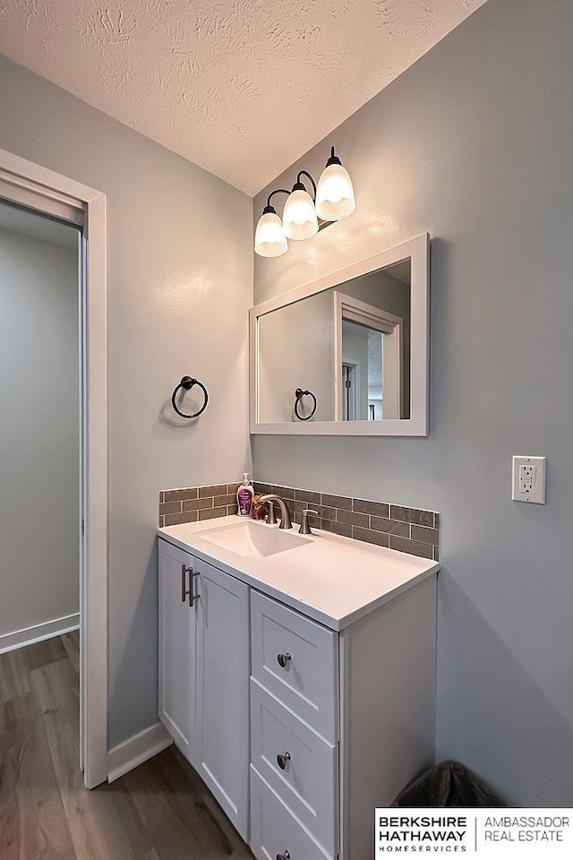 bathroom featuring vanity, a textured ceiling, baseboards, wood finished floors, and backsplash