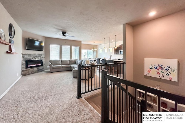 interior space featuring a fireplace, baseboards, a textured ceiling, carpet, and ceiling fan with notable chandelier