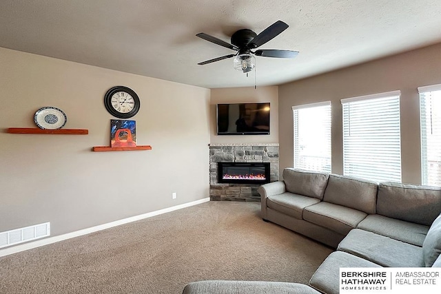 living room featuring visible vents, carpet floors, baseboards, a stone fireplace, and ceiling fan
