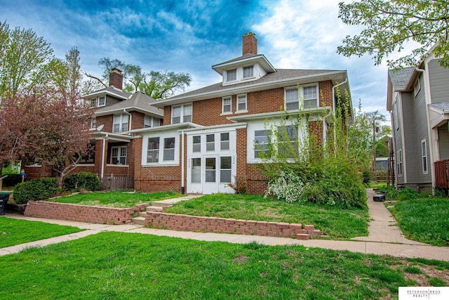 view of front of property featuring a chimney, a front yard, and brick siding