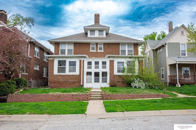 american foursquare style home with brick siding, a chimney, and a front lawn