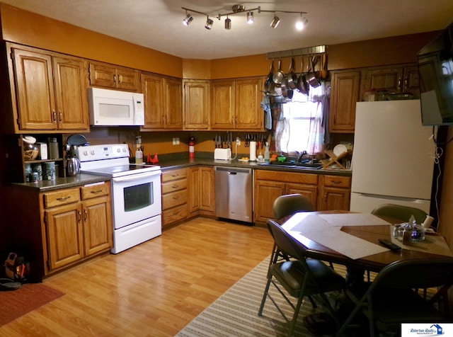 kitchen featuring brown cabinetry, a sink, dark countertops, and white appliances