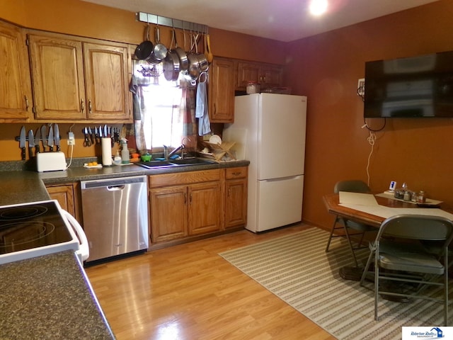 kitchen featuring dark countertops, dishwasher, a sink, freestanding refrigerator, and light wood finished floors