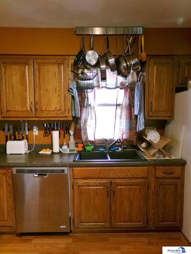 kitchen featuring stainless steel dishwasher, a sink, brown cabinetry, and dark countertops