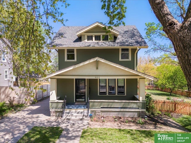 american foursquare style home featuring a porch, fence, and roof with shingles