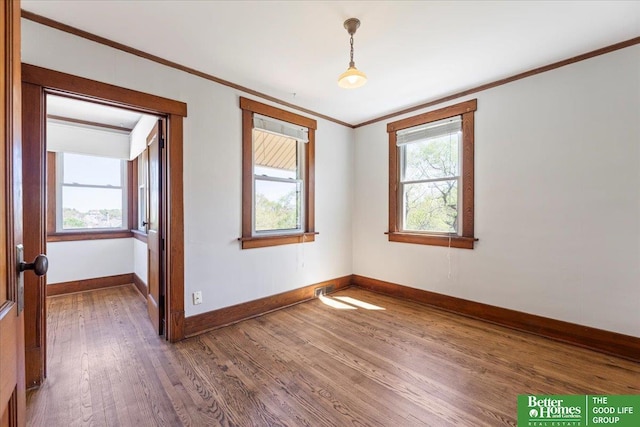 spare room featuring crown molding, baseboards, and wood finished floors