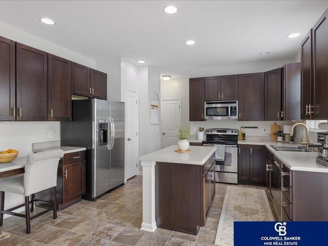 kitchen with dark brown cabinets, a sink, light countertops, stainless steel appliances, and a kitchen island