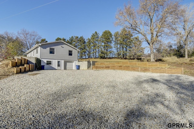 view of home's exterior with an attached garage, fence, and gravel driveway