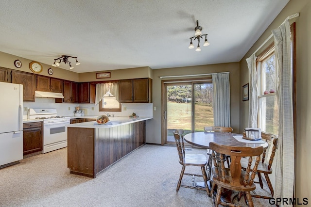 kitchen featuring a textured ceiling, light countertops, a peninsula, under cabinet range hood, and white appliances