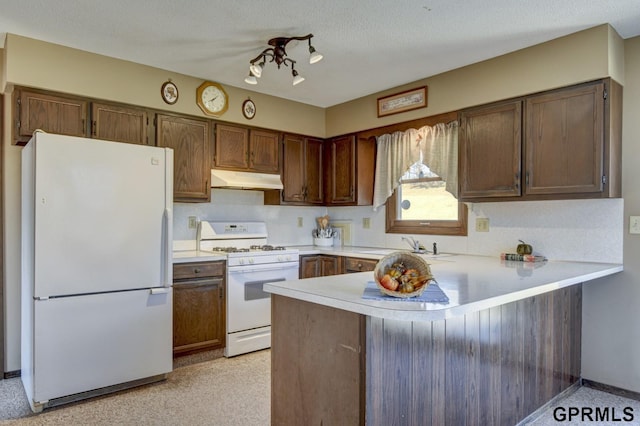 kitchen with a peninsula, white appliances, light countertops, under cabinet range hood, and a sink