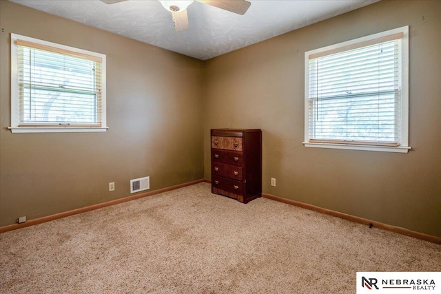 empty room with visible vents, carpet, ceiling fan, and a healthy amount of sunlight