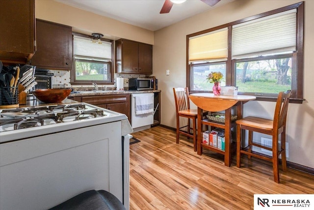 kitchen with dark brown cabinetry, light wood-style flooring, a ceiling fan, white range with gas stovetop, and tasteful backsplash