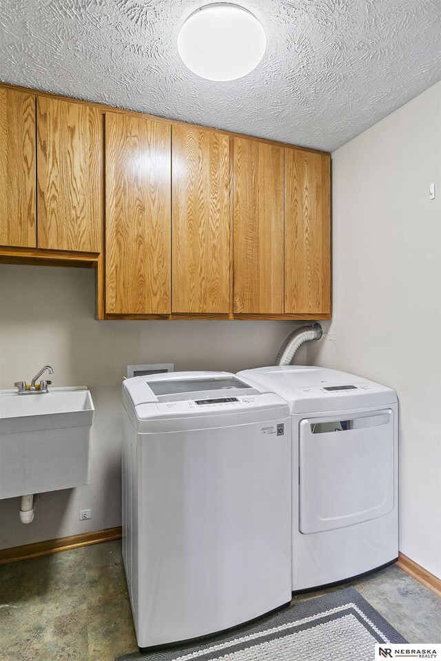 laundry area with baseboards, washer and clothes dryer, a textured ceiling, a sink, and cabinet space