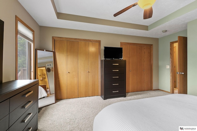 bedroom featuring two closets, a ceiling fan, light carpet, and a raised ceiling