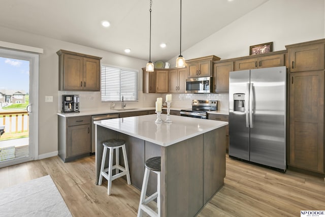 kitchen with a kitchen breakfast bar, backsplash, appliances with stainless steel finishes, light wood-type flooring, and a sink