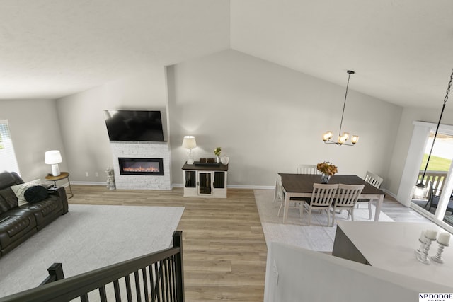 living area featuring a fireplace, a chandelier, light wood-style flooring, baseboards, and lofted ceiling
